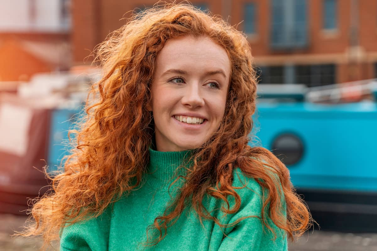 Woman with red curly hair smiling and looking off to the side